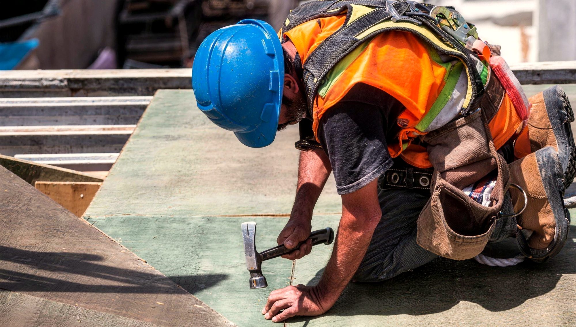 A roofer in a hi-vis vest hammering on a roof deck