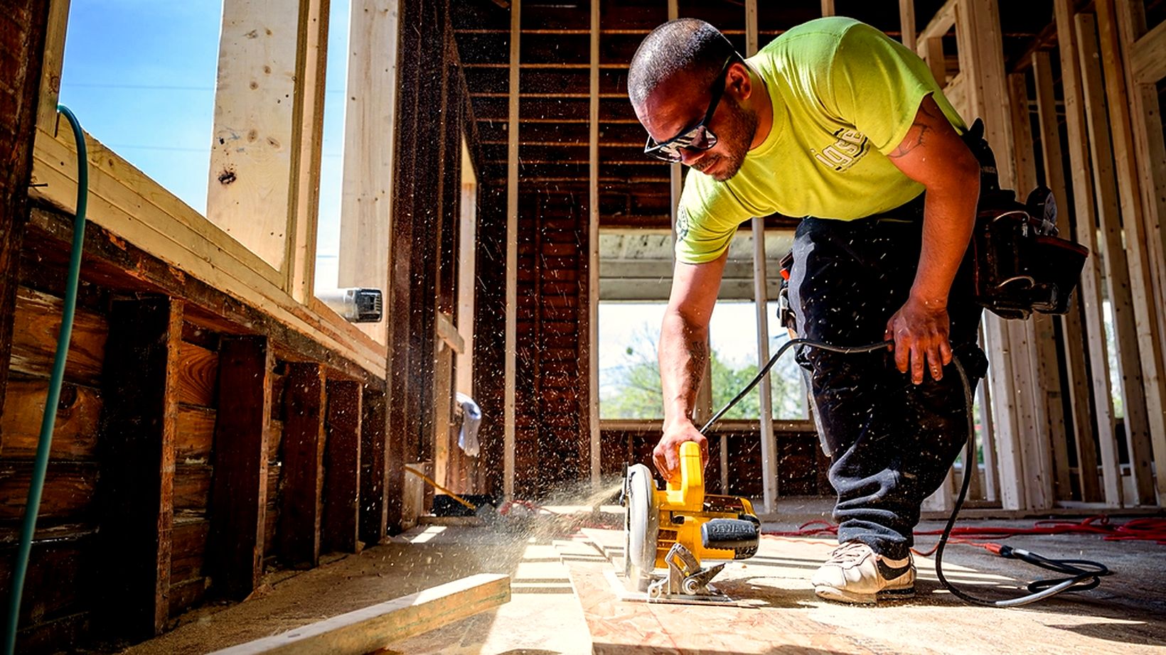 A renovation contractor cutting sheathing with a circular saw, sawdust in the air